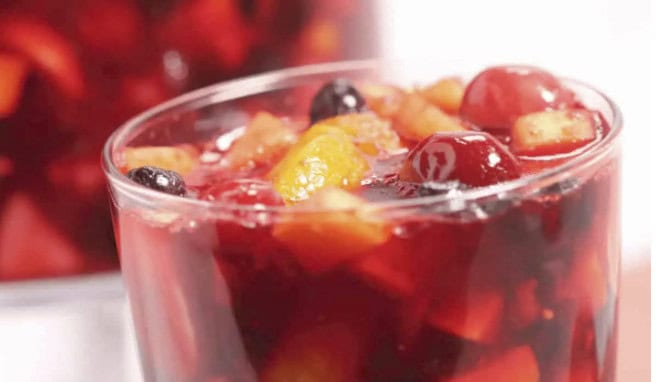 A close-up of a glass filled with red fruit punch containing chopped fruit pieces, such as grapes, apples, and oranges—perfect for sipping at your next backyard barbecue.